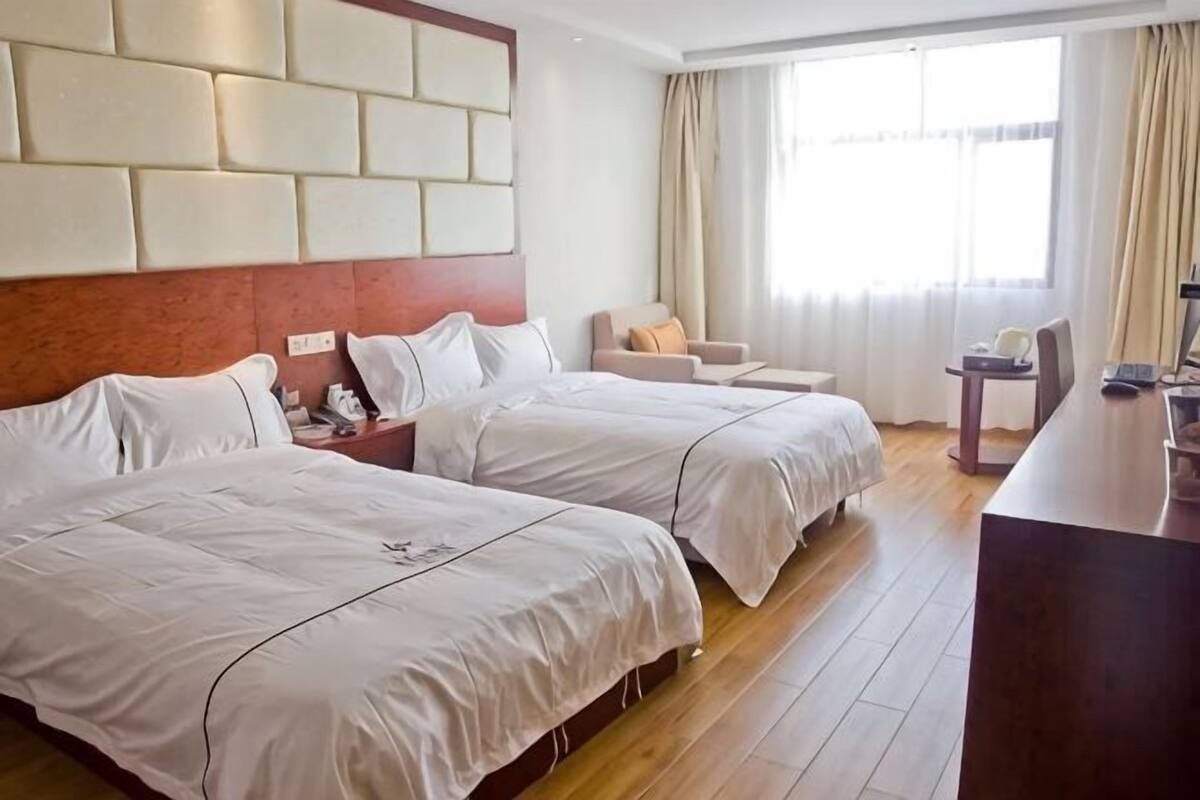 Une chambre d’hôtel avec deux lits, un bureau, une chaise et une grande fenêtre.