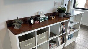 Un meuble de rangement blanc, doté de plusieurs compartiments, d’une étagère supérieure en bois et d’une fenêtre donnant sur des bâtiments.