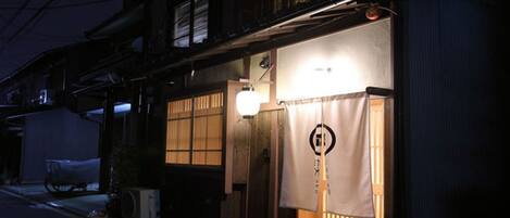 Un edificio tradicional japonés con entrada iluminada, puertas correderas y un letrero con caracteres japoneses.