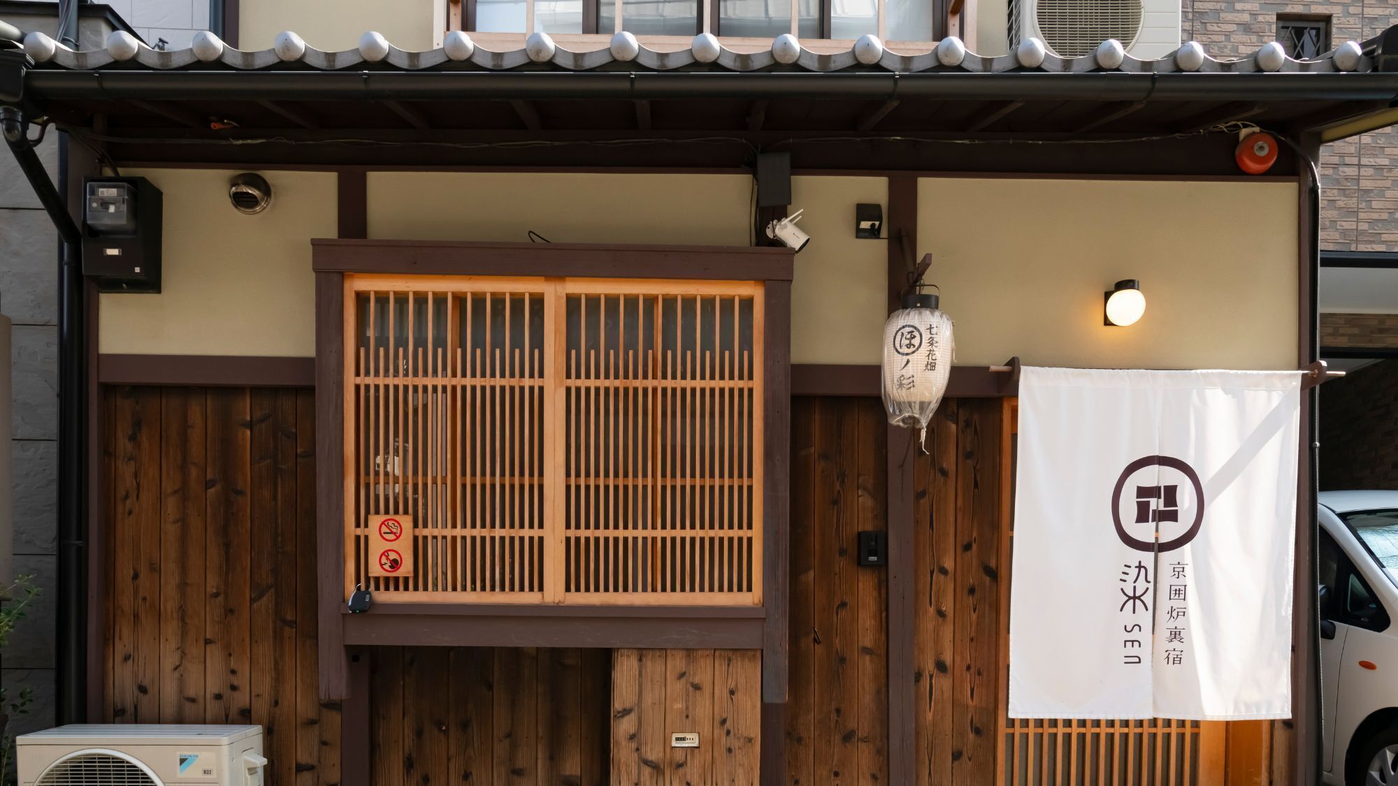 Ein traditionelles japanisches Gebäude mit einem Holztor, einer Laterne und einem Schild mit japanischen Schriftzeichen.