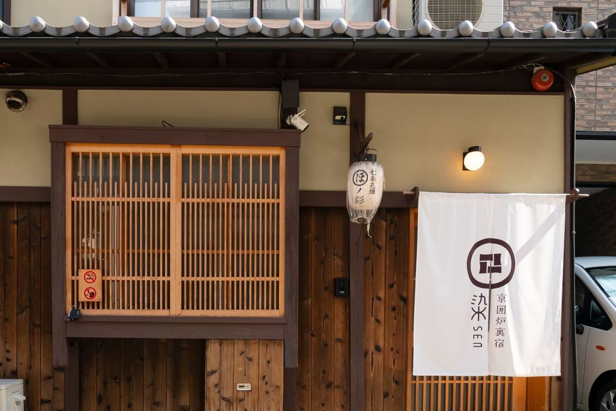 Ein traditionelles japanisches Gebäude mit einem Holztor, einer Laterne und einem Schild mit japanischen Schriftzeichen.