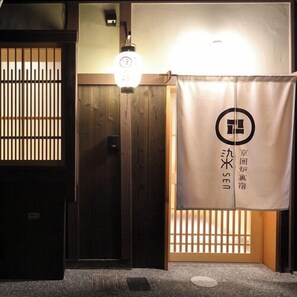 Une entrée de style japonais traditionnel, avec des portes en bois, une lanterne et une bannière ornée de caractères japonais.