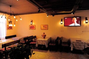 A restaurant with tables and chairs, a television screen, and wall-mounted lights.