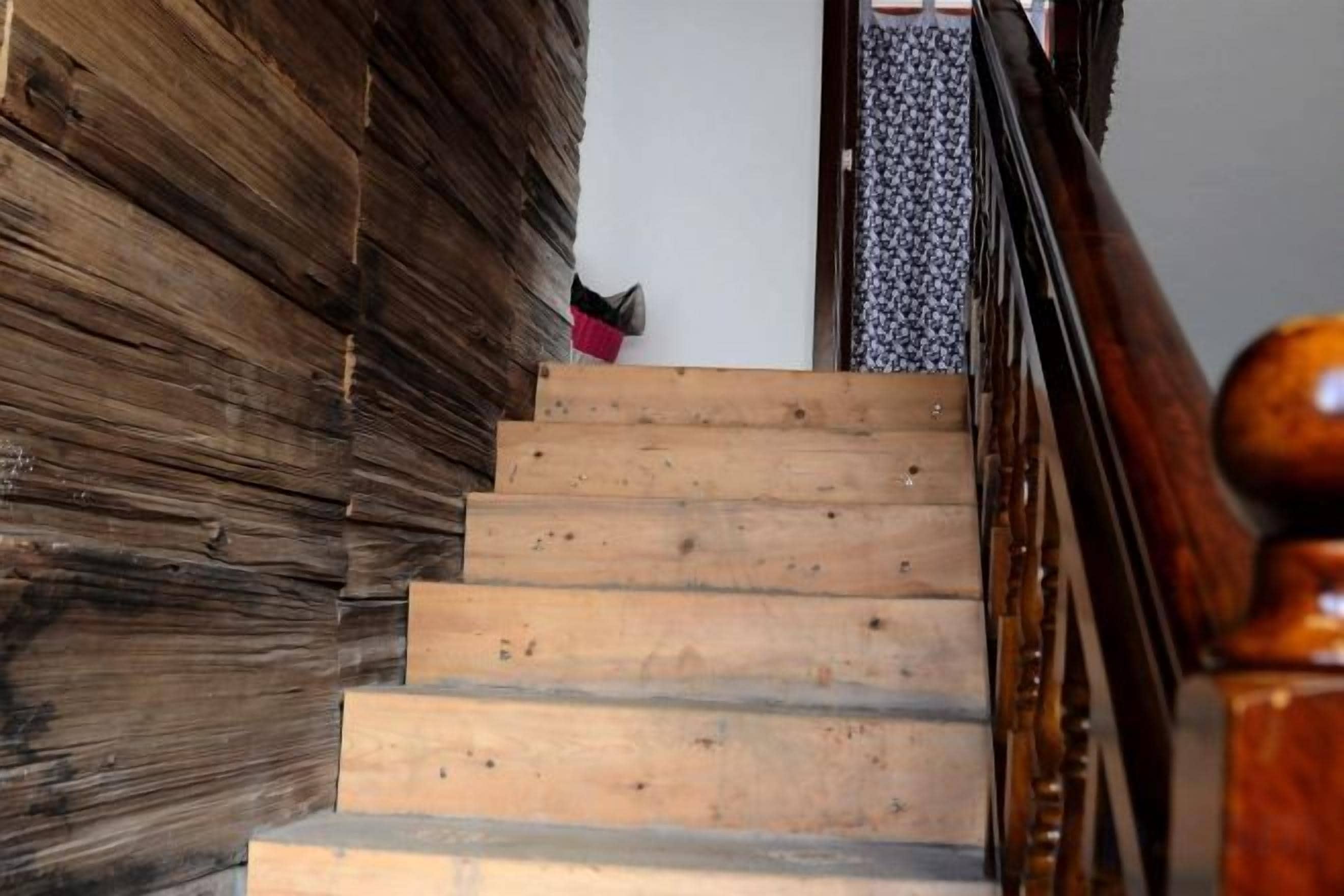 Una escalera de madera con barandilla que lleva a una puerta con cortina decorada.