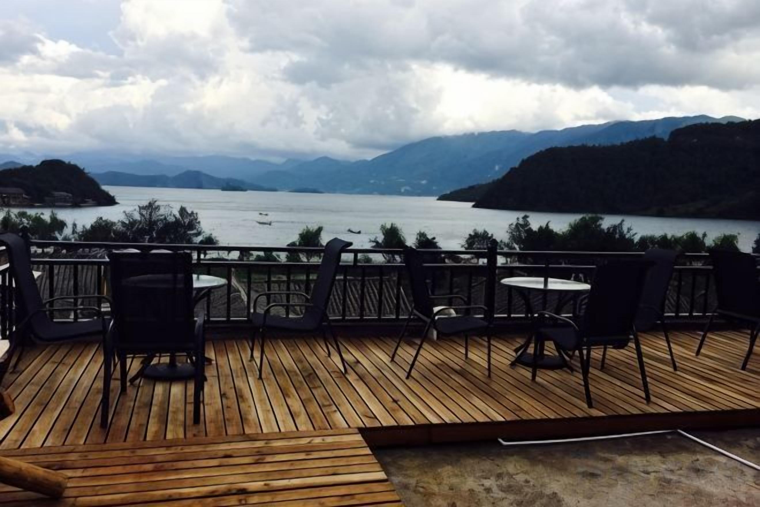 Una terraza de madera con asientos al aire libre, con vistas a un lago y montañas.