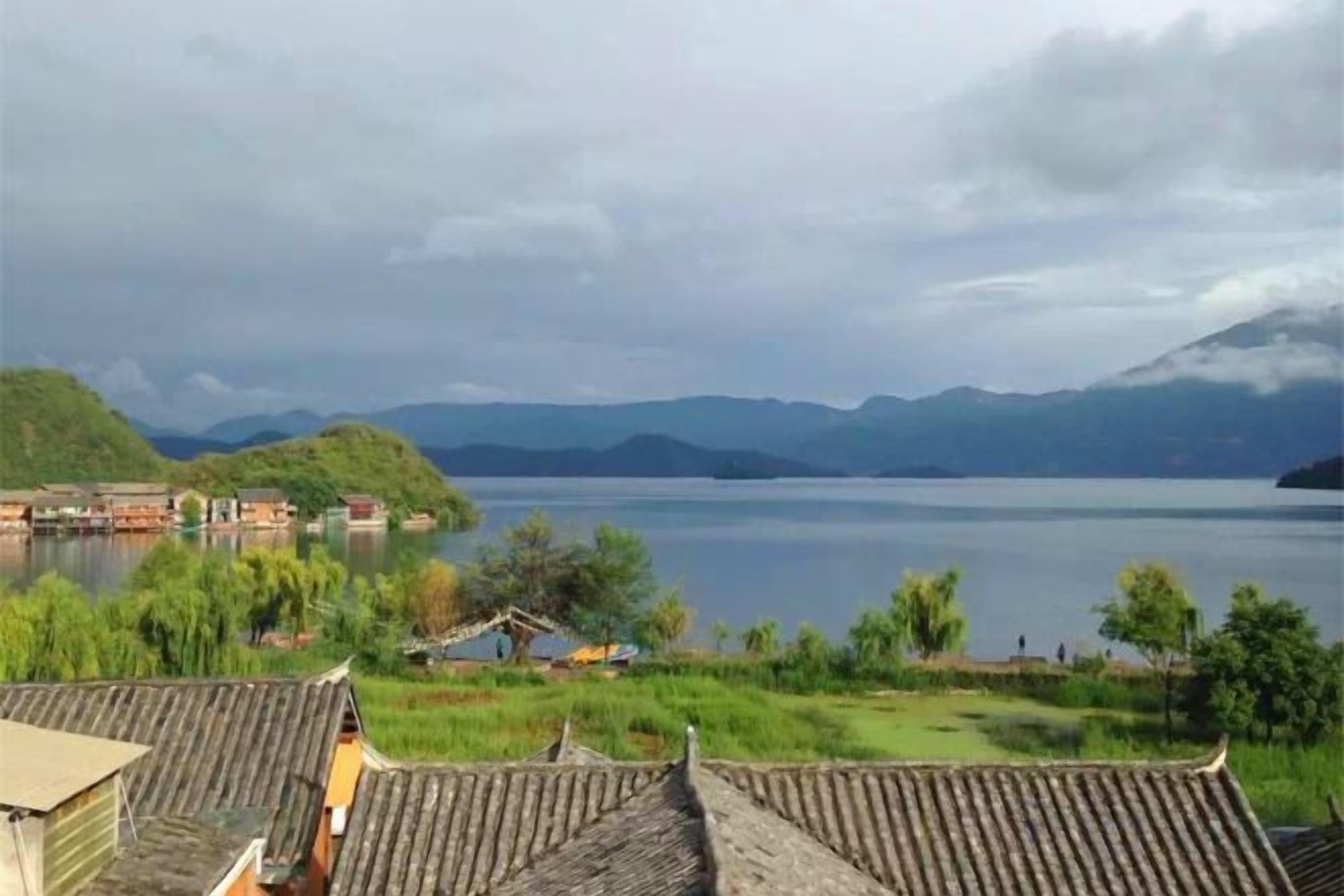 Un village traditionnel avec des maisons à étages donnant sur un lac paisible et des montagnes lointaines.