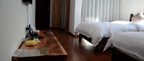 A room with two beds, a wooden table with a menu, and a TV mounted on the wall.