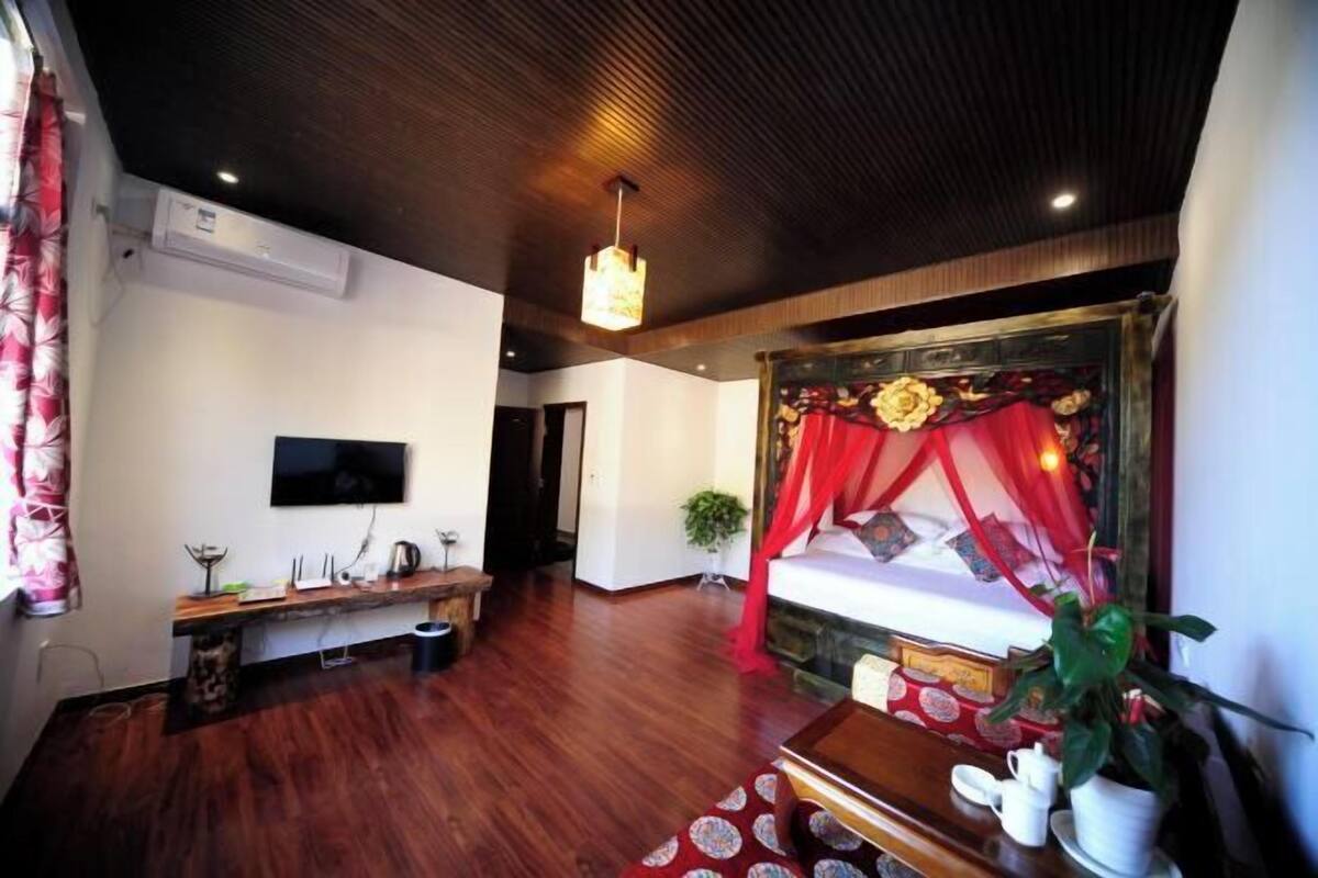 Una habitación con una cama, televisión, banco de madera y una cama con dosel rojo.