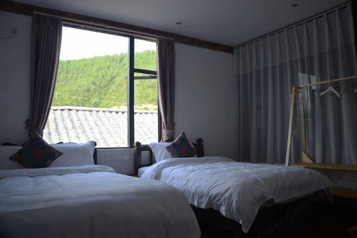 Habitación de hotel con dos camas, una ventana con cortinas y vistas a un paisaje verde.