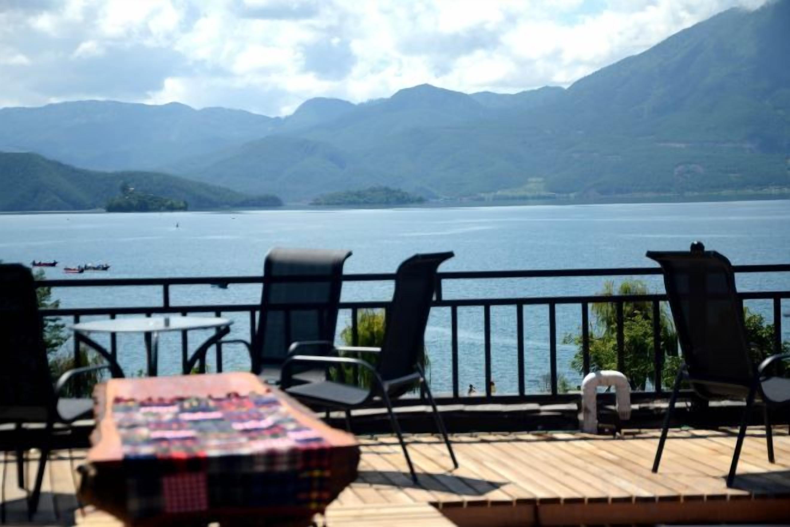 Eine Terrasse mit Stühlen und Tisch, die auf einen See mit Bergen im Hintergrund blickt.
