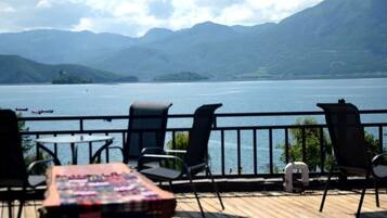 Eine Terrasse mit Stühlen und Tisch, die auf einen See mit Bergen im Hintergrund blickt.