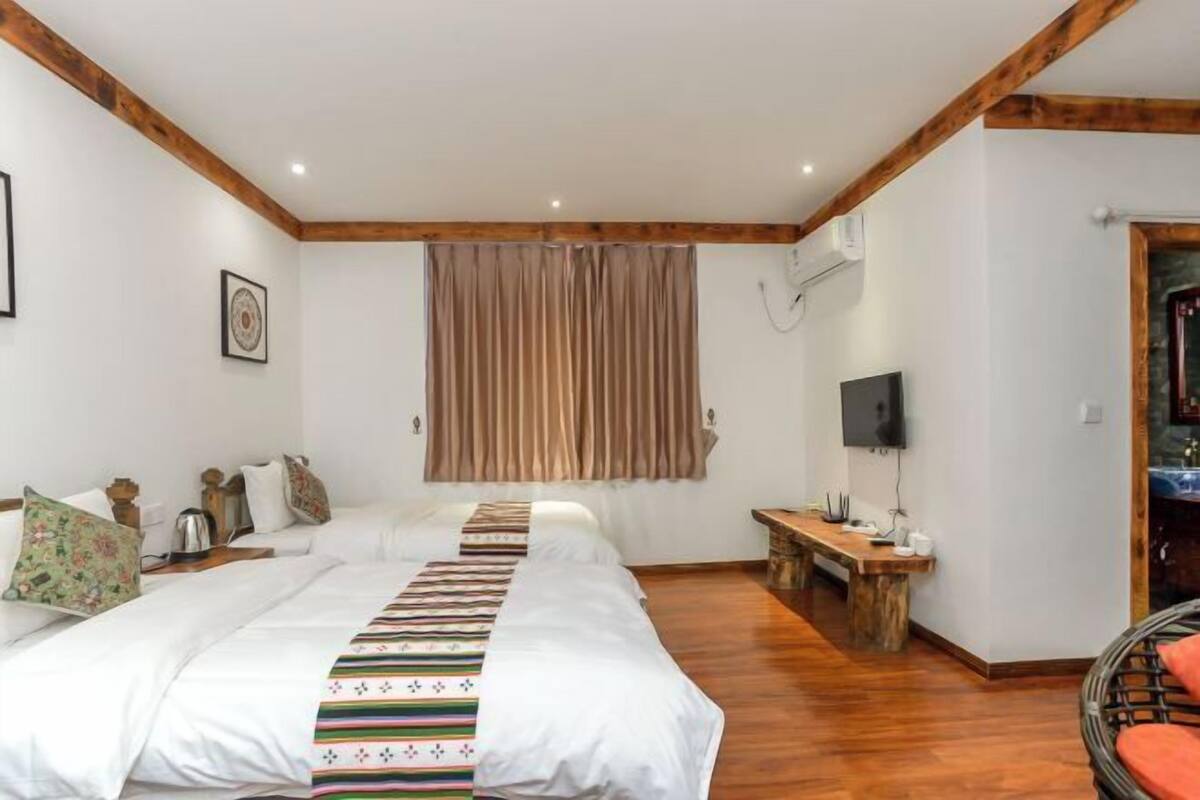 Un dormitorio con dos camas, un banco de madera, un televisor y una ventana con cortinas.