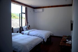 Una habitación con dos camas, una mesa de madera y una ventana con vistas al verdor.