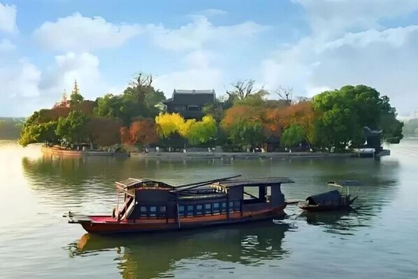 A traditional boat on a calm river with a temple and trees in the background. - HanTing Hotel (Jiaxing Nanhu Yaohan Shopping Mall Area) (Jiaxing)