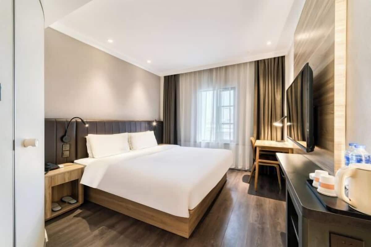 A modern hotel room with a large bed, bedside table, and a flat-screen TV.