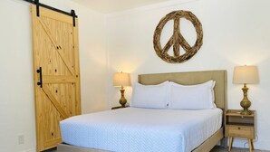 Een slaapkamer met een bed, twee nachtkastjes met lampen, een houten garderobe en een vredesteken decoratie aan de muur.