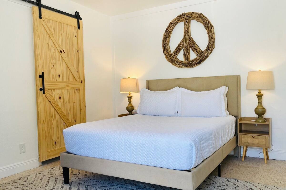 Un dormitorio con una cama, dos mesitas de noche con lámparas, un armario de madera y un adorno con el símbolo de la paz en la pared.