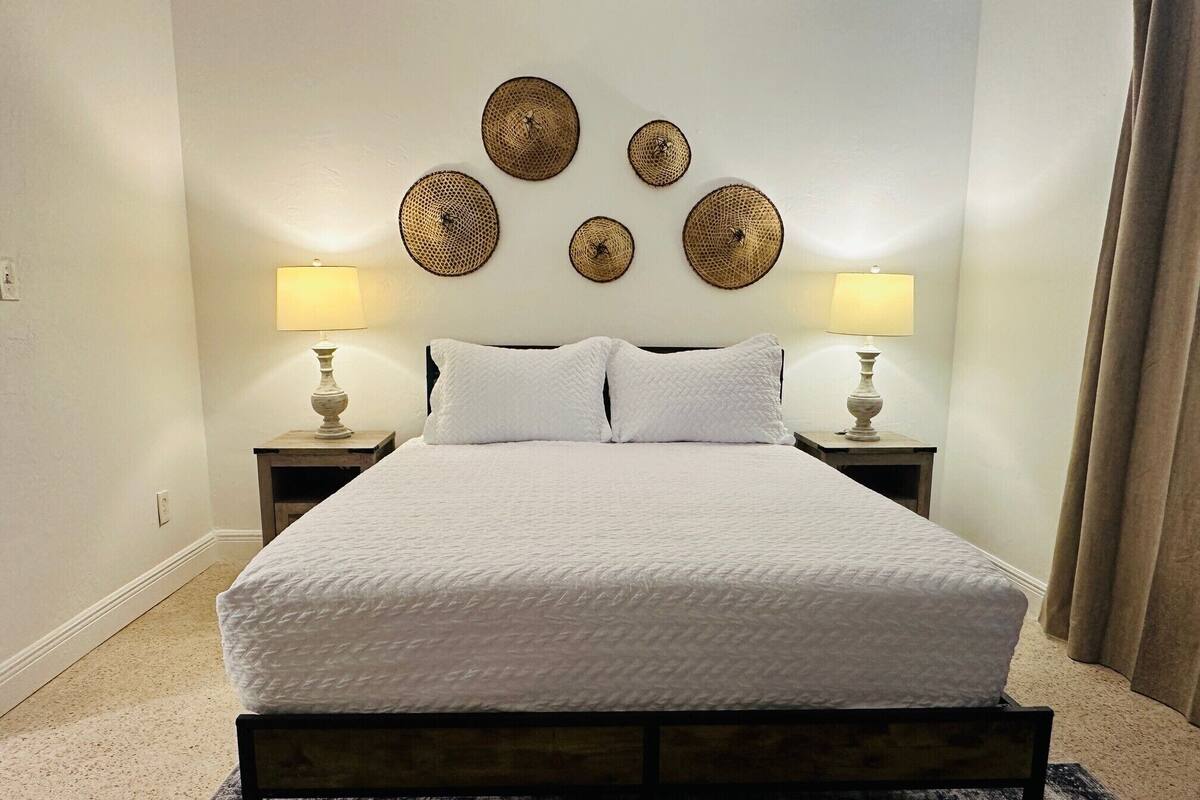 Una cama bien hecha con sábanas blancas, dos lámparas de noche y un cabecero con detalles decorativos.