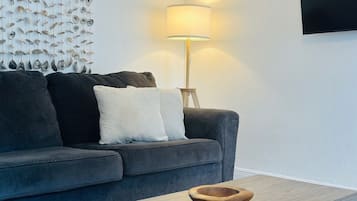 A modern living room with a grey sofa, white cushions, a wooden coffee table, and a wall-mounted lamp.