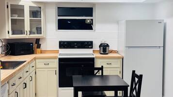 A compact kitchen with white cabinets, a black stove, a microwave, a refrigerator, and a dining table with chairs.