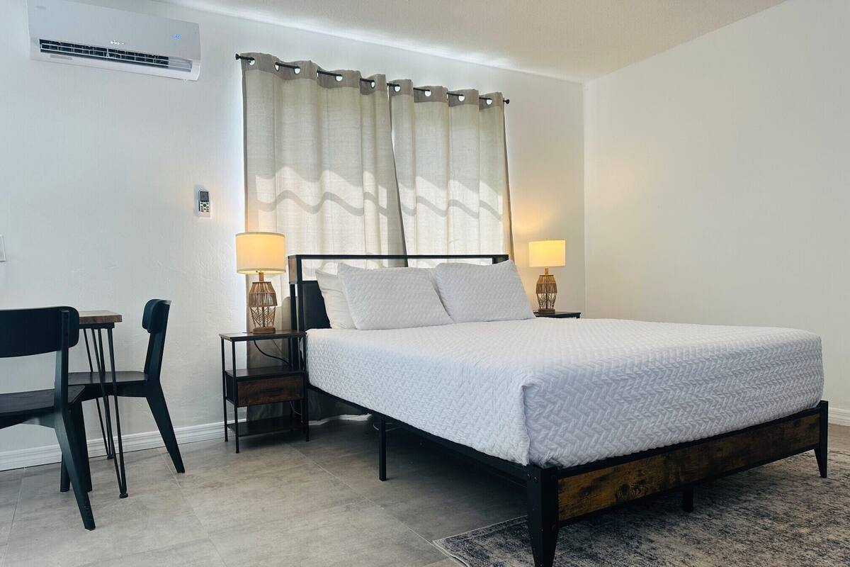 Un dormitorio con cama, mesitas de noche, una silla y un escritorio.