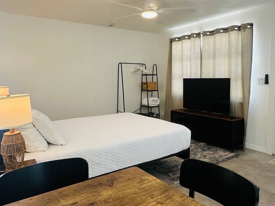A hotel room with a bed, a TV, a lamp, a shelf with towels, and a door.