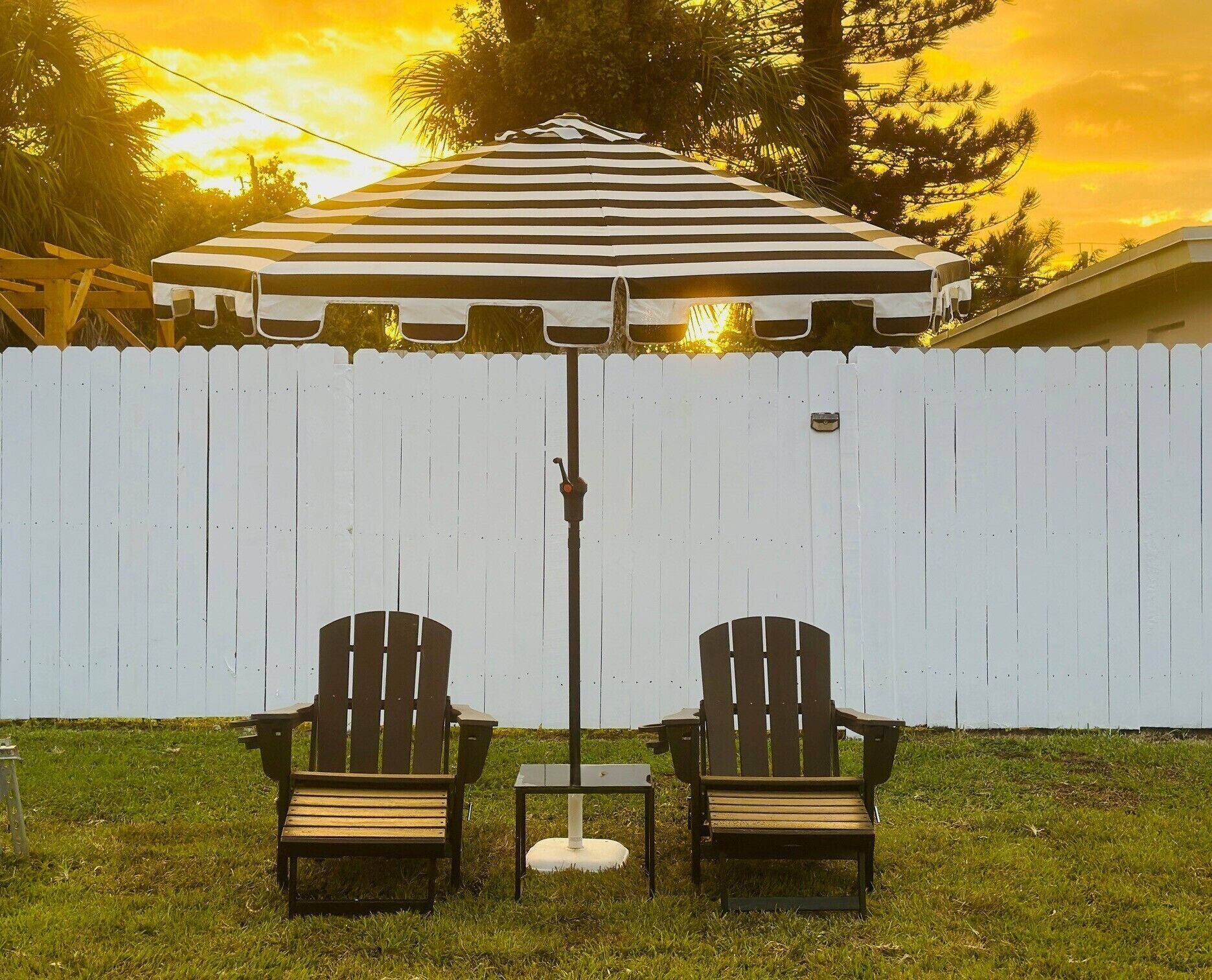 A patio area with two Adirondack chairs and a striped umbrella.