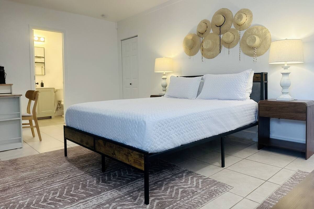 Un dormitorio con cama, lámparas de noche, un adorno de sombrero en la pared y una silla.