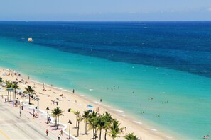 A beach with clear turquoise waters, palm trees, and a wide promenade.
