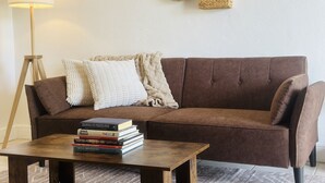 Een bruine bank met een witte deken en een stap boeken op een houten bijzettafeltje.