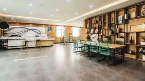 A modern hotel lobby with a reception desk, seating area, and a bookshelf filled with books and awards. - Shankee Tea Style (Ancient City of Kashgar Xiyu Avenue Food Street) (Kashgar City)