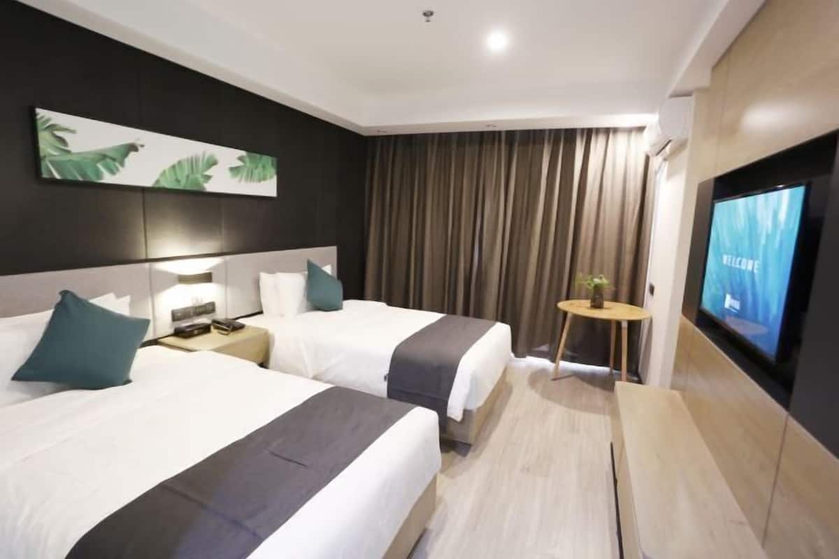 A hotel room with two beds, a TV, a small table with a plant, and a painting on the wall.