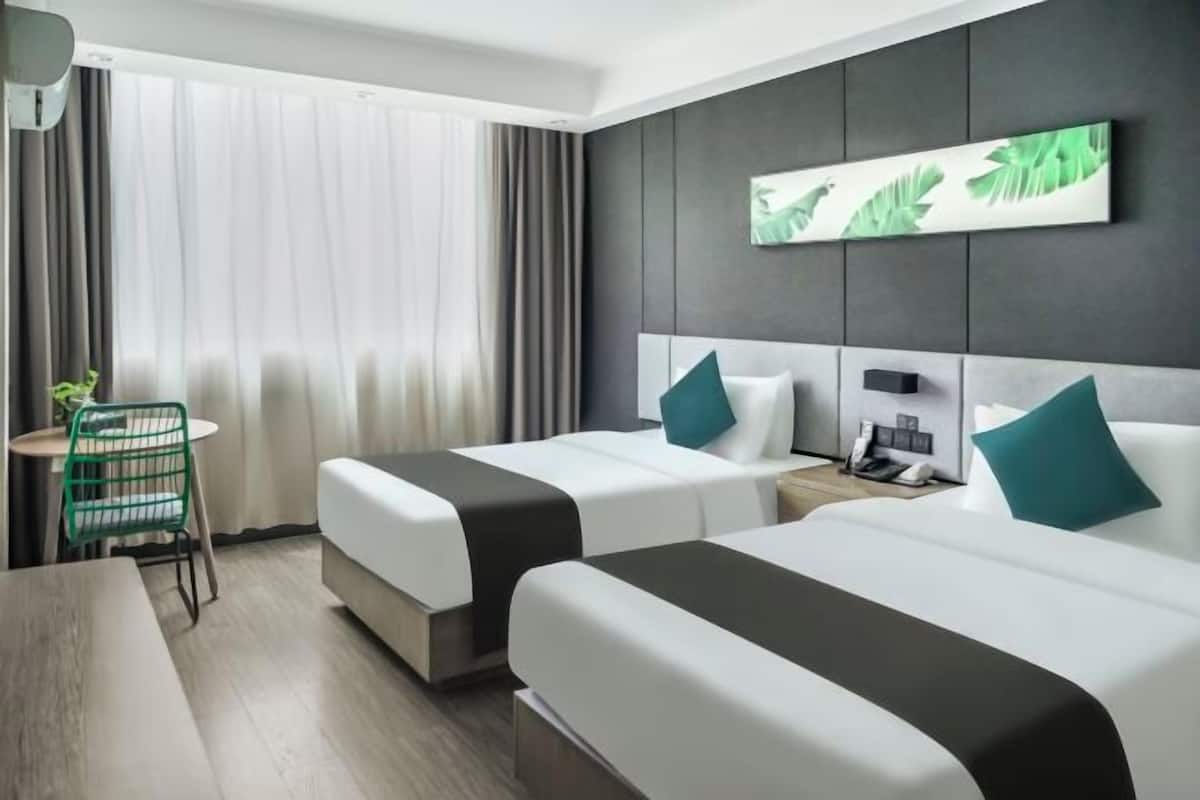 A hotel room with two beds, a desk, a chair, and a large window with curtains.