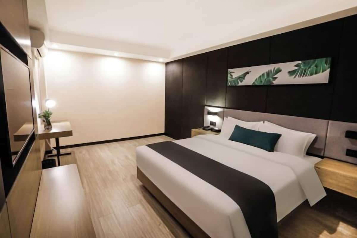 A modern hotel room with a large bed, a bedside table, a nightstand, and a wall-mounted artwork.