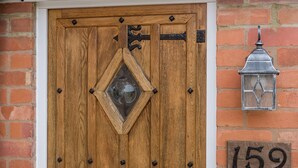 Une porte en bois ornée d’une fenêtre en forme de losange, une lanterne en métal et le numéro de la maison, « 159 », peint sur le mur.