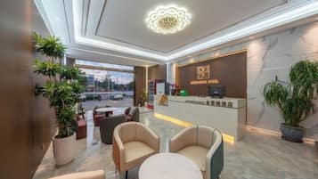 A hotel lobby with a reception desk, seating area, and large windows.