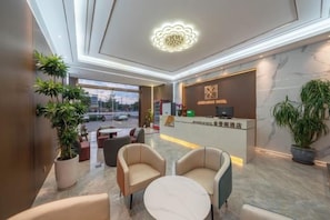A hotel lobby with a reception desk, seating area, and large windows.