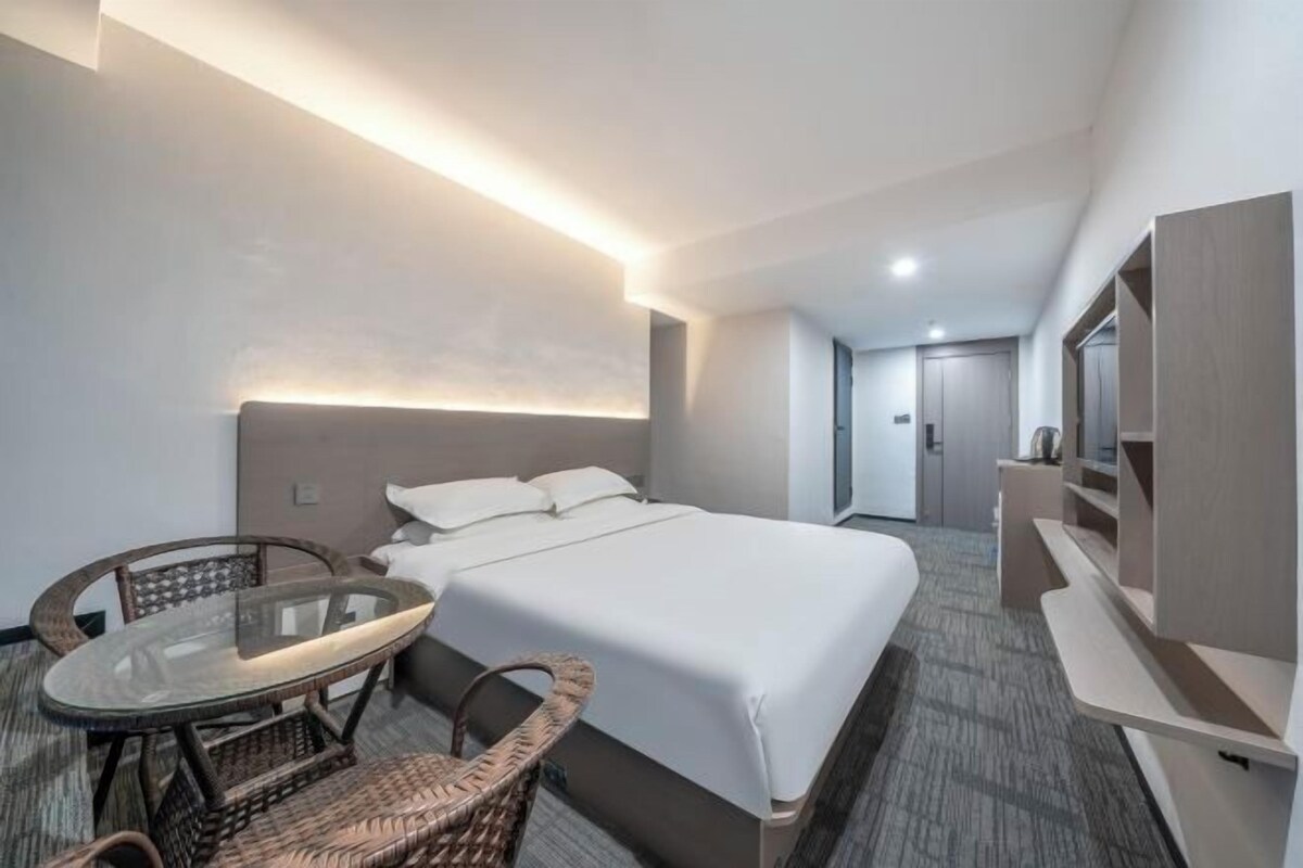 A hotel room with a bed, a glass-top table with chairs, a TV, and a wardrobe.