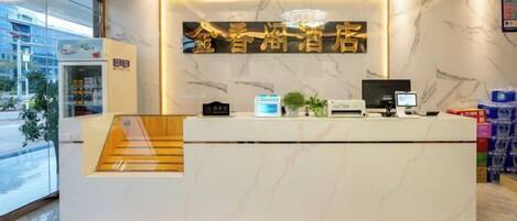 A hotel reception desk with a marble counter, a computer, and a staircase leading to an upper level.
