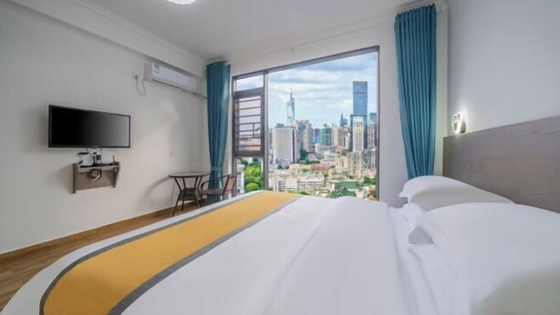 Habitación de hotel con cama, televisor, escritorio y vista a la ciudad.