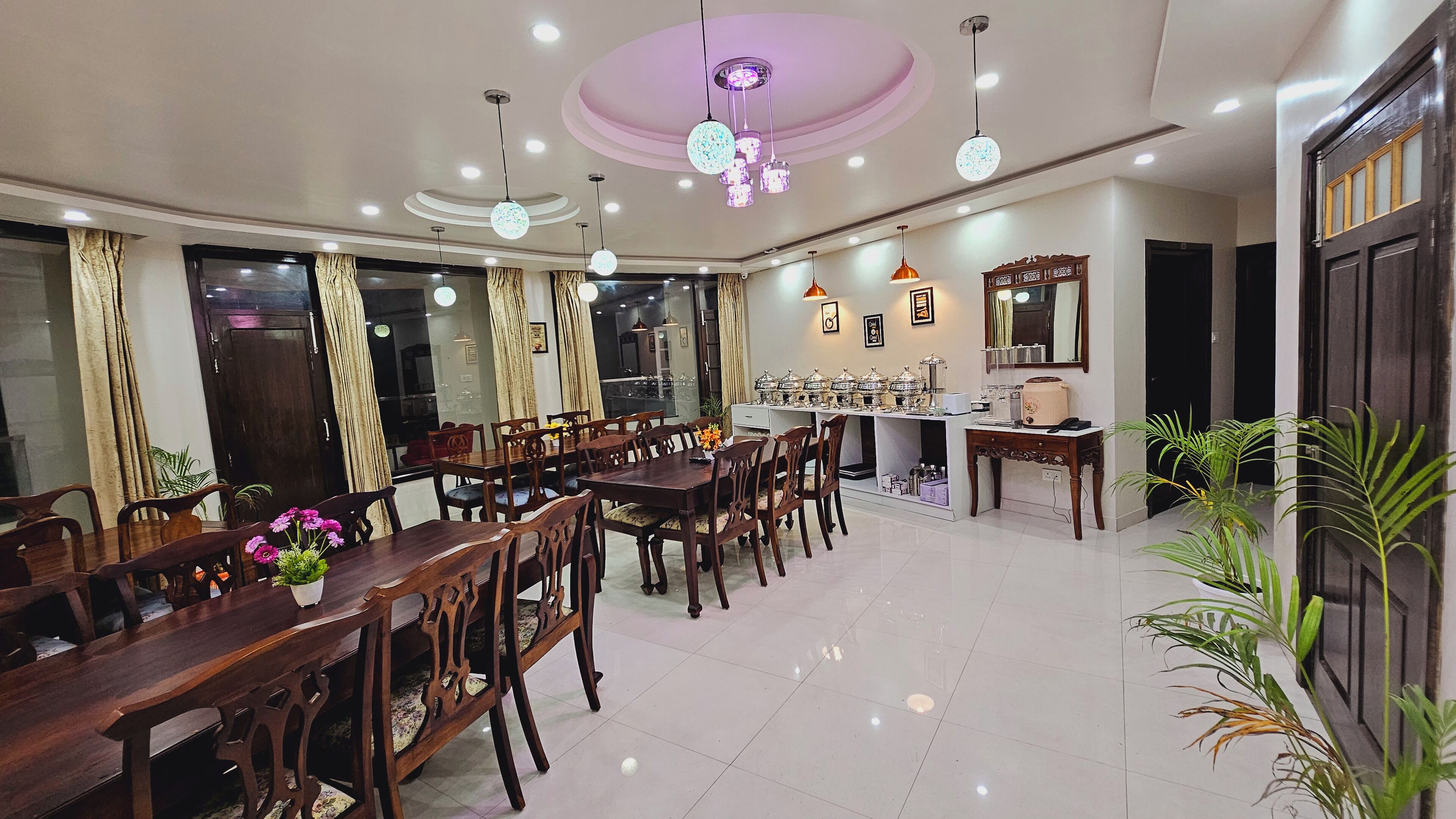 Un grand espace dédié à la salle à manger, avec des tables et des chaises en bois, un buffet et des luminaires modernes au plafond.