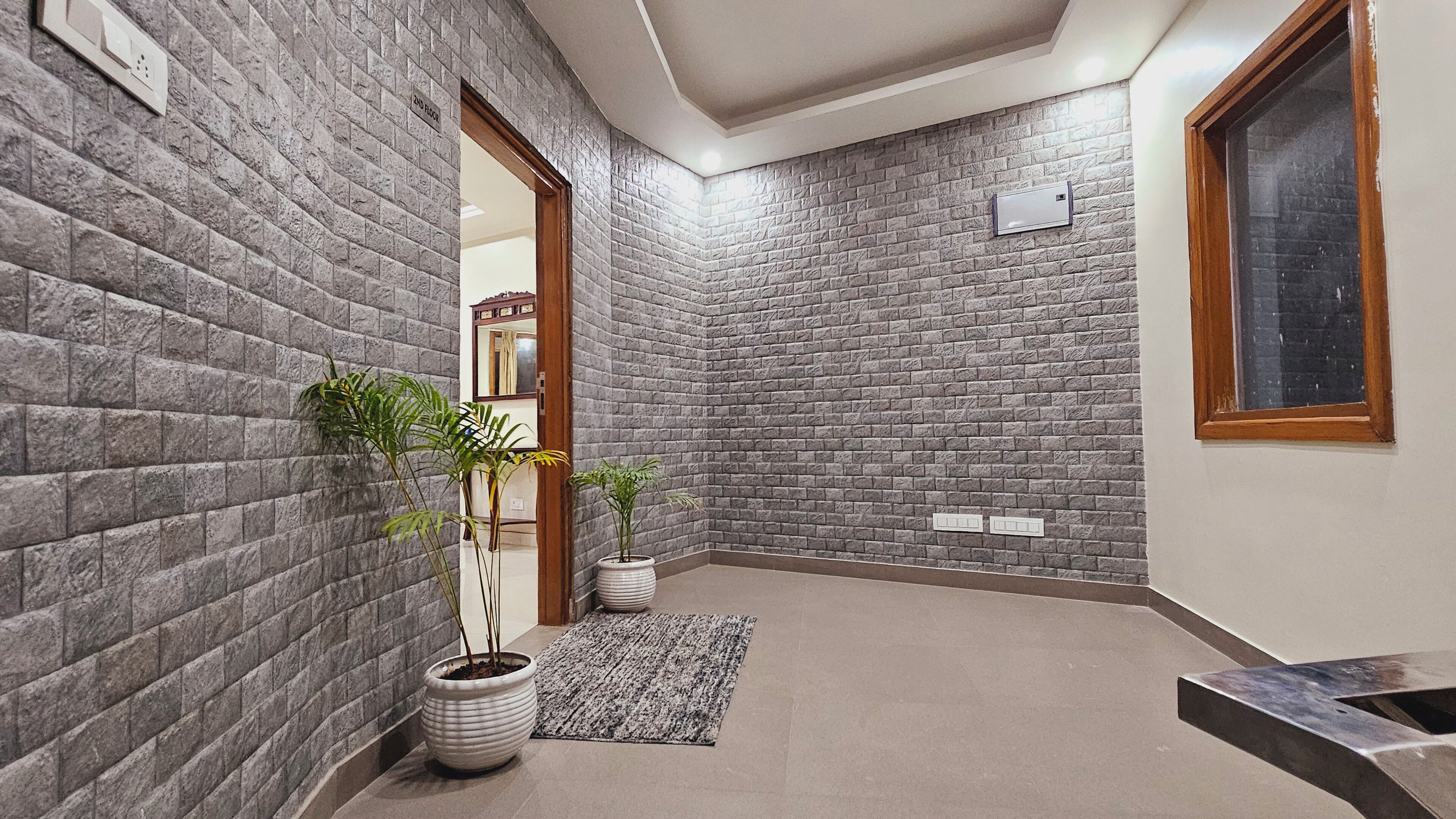 A modern bathroom with a brick wall design, a wooden door, and two potted plants.