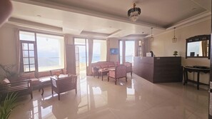 Ein geräumiger Wohnbereich mit einer Couch, einem Couchtisch und einer Rezeption. Große Fenster bieten einen Blick ins Freie.