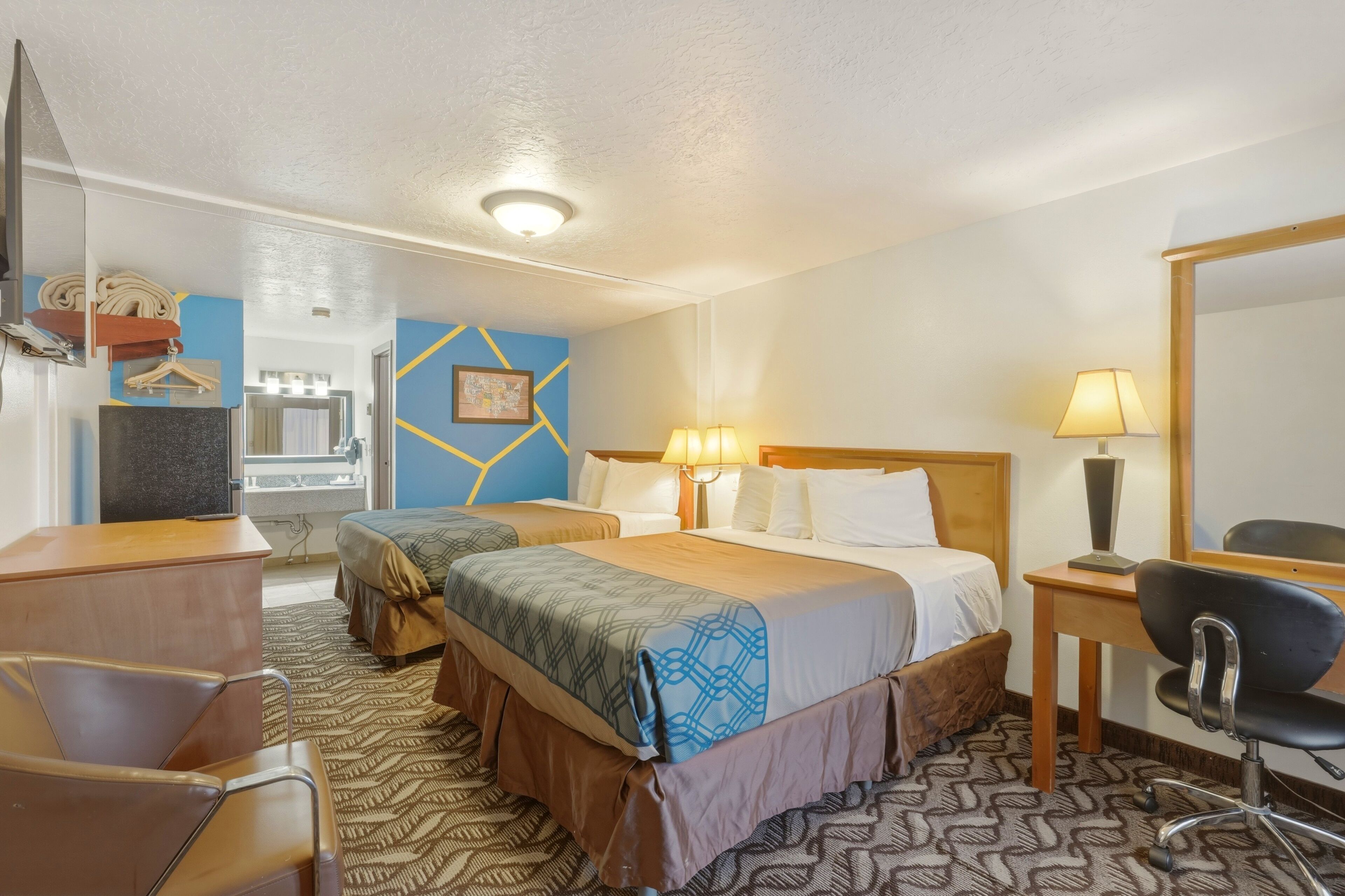 A hotel room with two beds, a desk, a chair, a mirror, and a bathroom visible through an open door.