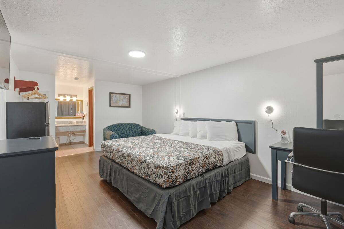 A bedroom with a bed, bedside table, chair, desk, and a mirror.