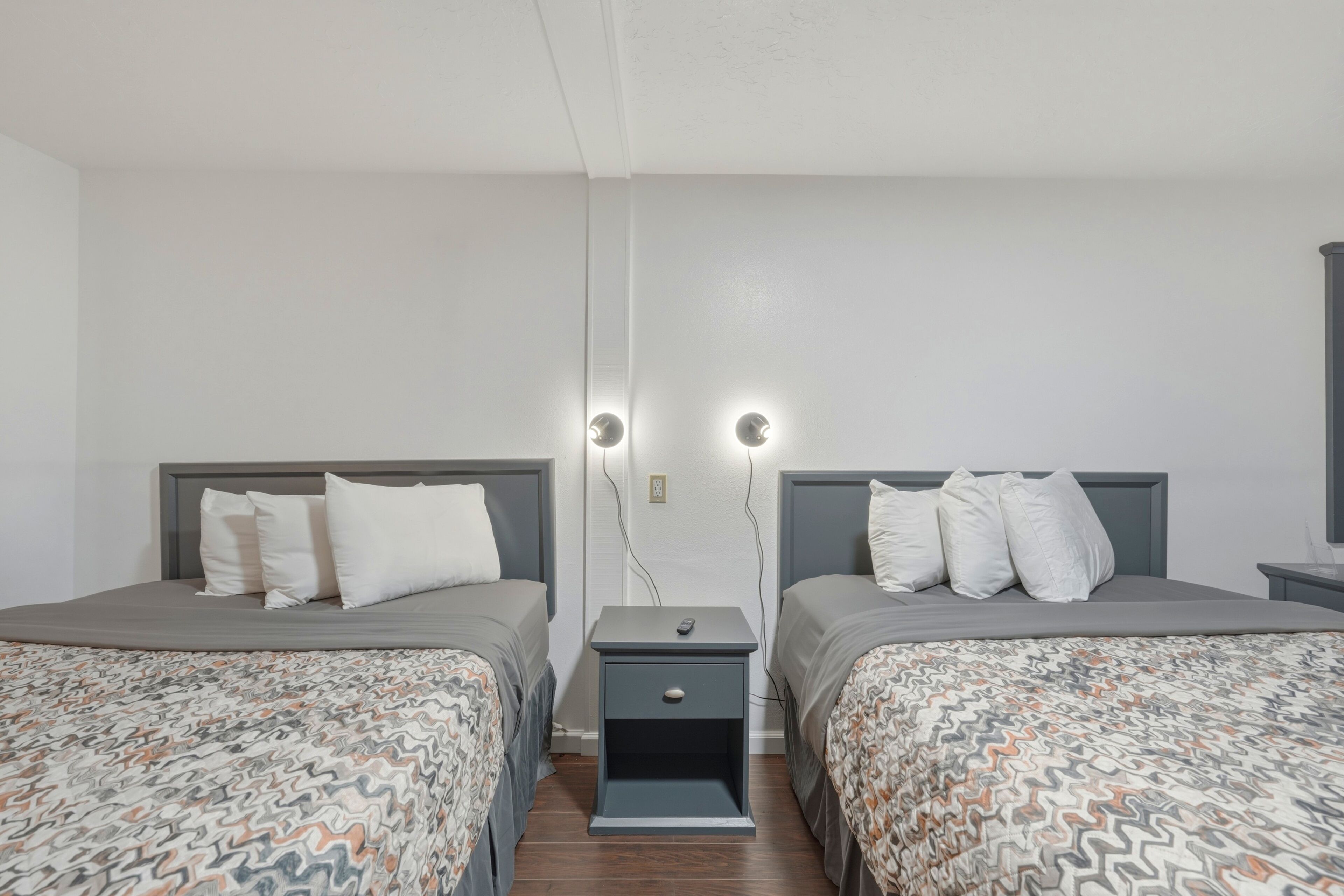 Habitación doble con dos camas, una mesita de noche con cajón y dos luces fijadas a la pared.