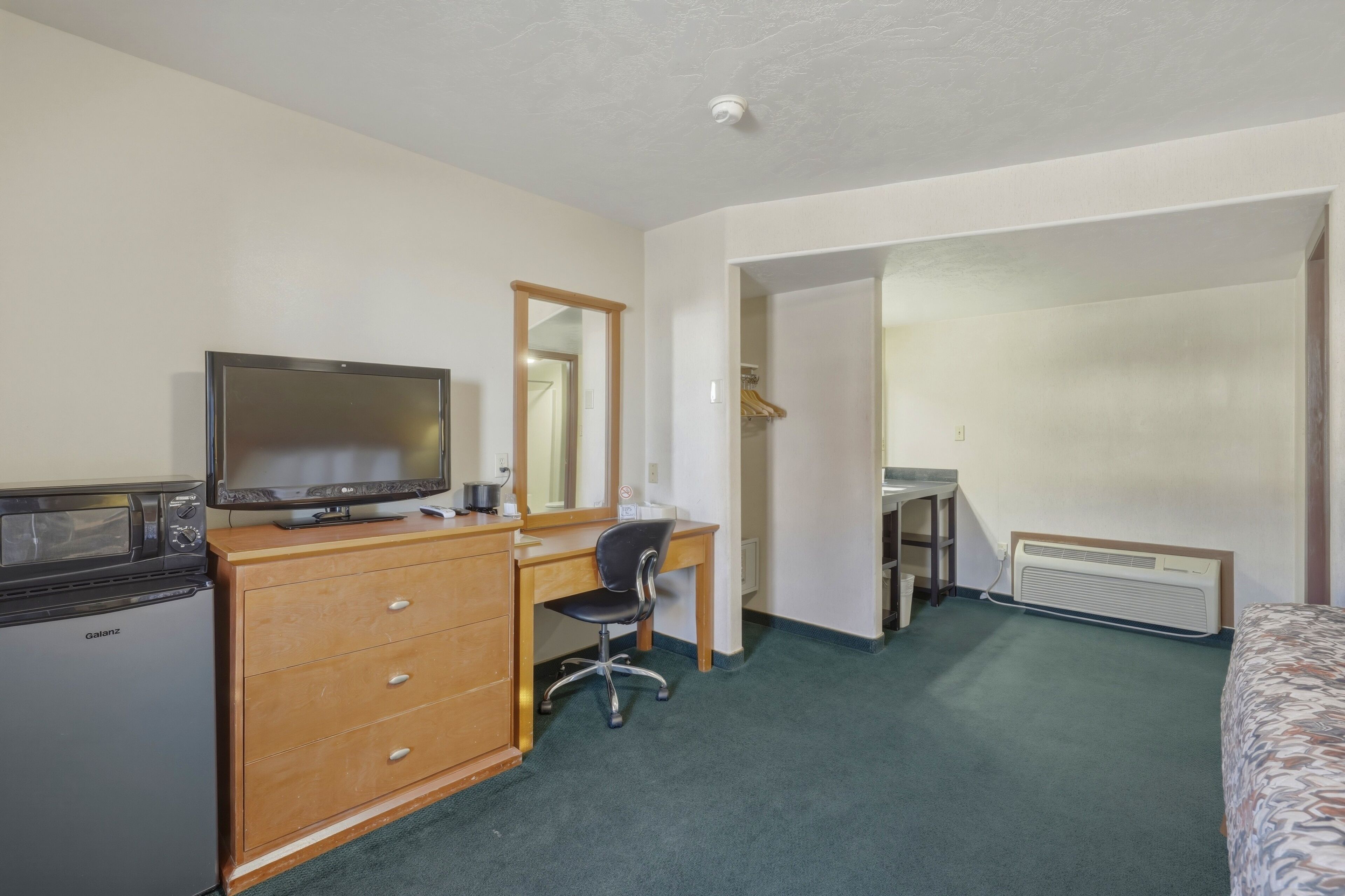 A hotel room with a bed, a desk with a chair, a television, a dresser, and a mirror.