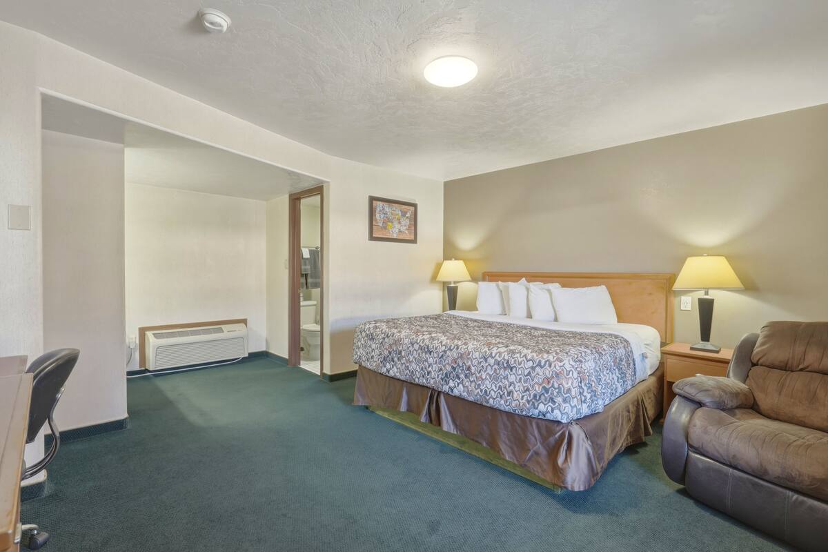 A hotel room with a bed, two bedside lamps, a chair, a desk, and a radiator.