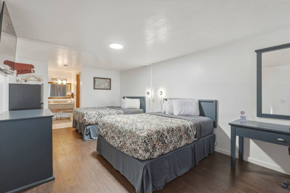 A hotel room with two beds, a desk, a dresser, and a bathroom visible through an open door.