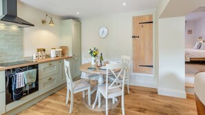 Une cuisine compacte avec un coin repas, un plancher en bois et une horloge visible au mur.